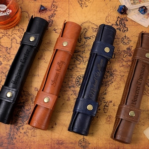 May include: Four personalised leather dice rolling trays. The trays are rolled up and have a brown, black, and blue leather exterior. Each tray has a name engraved on the side: Benjamin Carter, Shaun Kelly, Michael William, and Vincent Thomas.