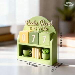 May include: A green wooden bookshelf-style desk organizer with the text "Books Read THIS YEAR". It displays the number "077" on rotating blocks. The organizer also features miniature books, a cup and saucer, and a potted succulent. Dimensions: 4.3" x 4.9" x 1.7".