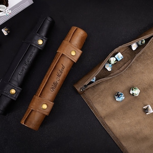 May include: Two brown leather dice rolling trays with personalized names, "Willie McLeod" and "Gary Eaton", and a brown leather dice bag with a zipper closure. The bag is filled with blue and white dice.