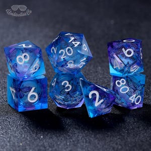 May include: Set of blue and purple dice with butterfly designs. The dice are made of clear plastic and have white numbers. The dice are on a black surface.