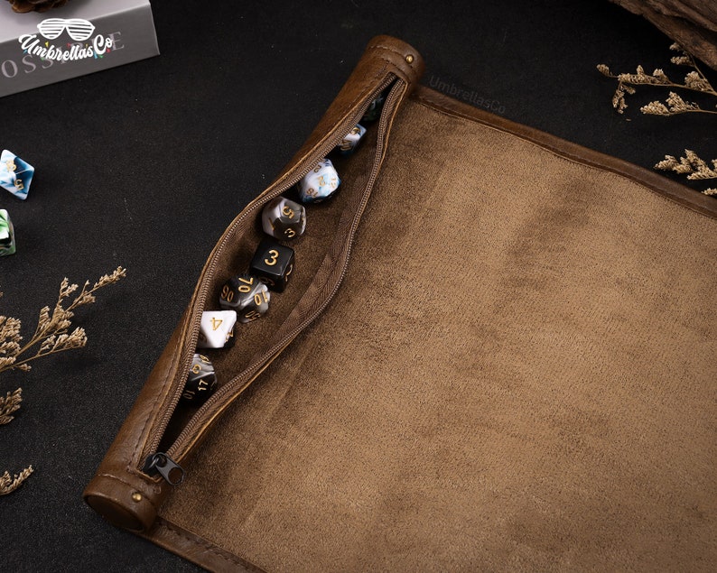 May include: A brown leather dice bag with a zipper closure. The bag is open and filled with various colored dice. The bag has the text "UmbrellasCo" printed on it.