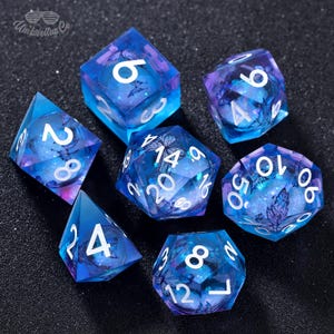 May include: Set of seven blue and purple dice with white numbers and butterfly designs. The dice are made of clear plastic with a glittery finish.