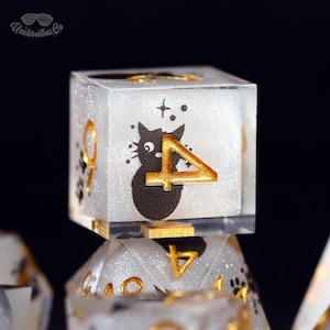 May include: A clear, glitter-filled dice with a black cat illustration and gold-colored numbers. The number "4" is prominently displayed. The dice are part of a set, with other dice visible in the background.