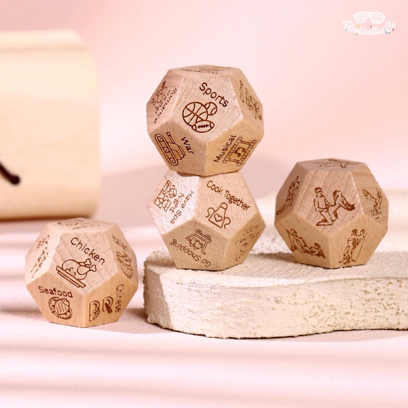 May include: Wooden dice with engraved illustrations and text. One die features sports and war icons, another has cooking and shopping images, and a third die displays chicken and seafood. The dice are light brown and have a geometric shape.