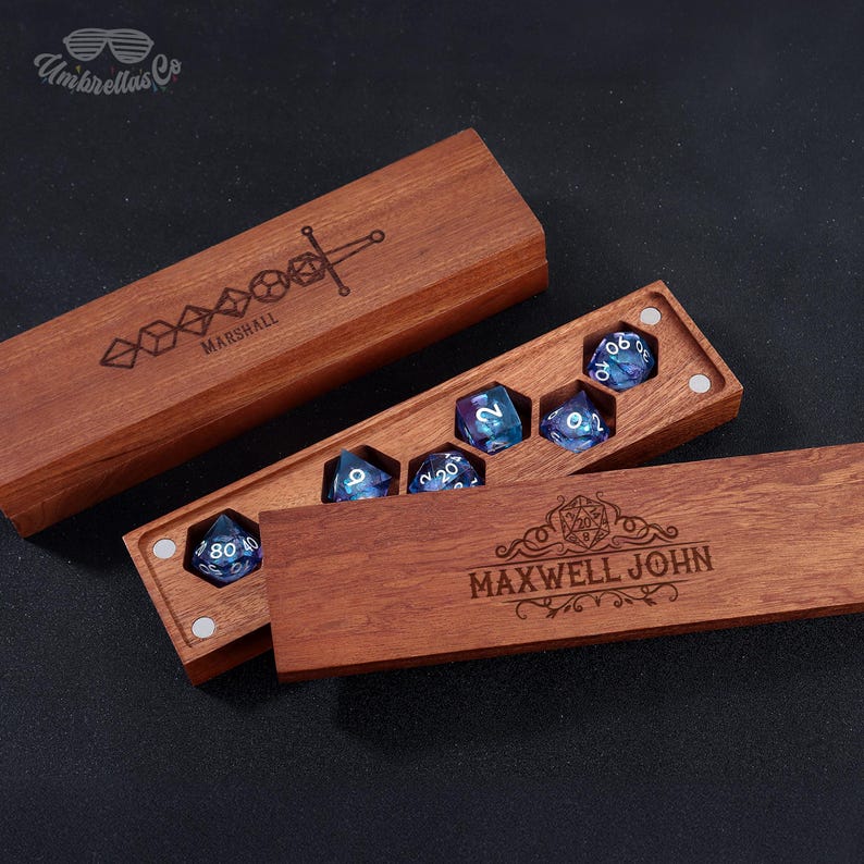 May include: A wooden box with a hinged lid, engraved with the name "MAXWELL JOHN" and a decorative design. The box contains a set of six iridescent dice with white numbers.