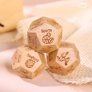 May include: Three wooden dice with engraved illustrations and text. One die features "Sports" with a basketball and football. Another shows "Seafood" with a fish. The third die has a person running. The dice are light brown.