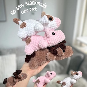 May include: A stack of three crocheted farm animal toys in white, pink, and brown. The toys are stacked on top of each other. The image also shows individual crocheted farm animal toys in the hands of a person. The text "No sew stackimals farm pack" is in the image.