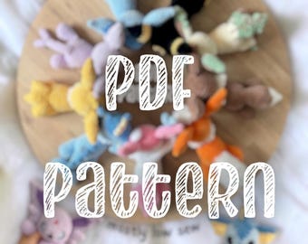 May include: A collection of small, colourful crocheted plush creatures arranged in a circle on a round wooden board. The text PDF PATTERN is overlaid in white. The creatures feature various colours including blue, yellow, black, pink, and purple.
