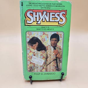 May include: A green paperback book titled "Shyness: What it is. What to do about it." by Philip G. Zimbardo. The cover features a photo of a couple standing in front of a patterned wall.