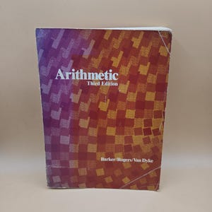 May include: A textbook titled "Arithmetic Third Edition" with a colorful cover. The cover transitions from purple to red with a checkered pattern. The authors' names, Barker/Rogers/Van Dyke, are printed at the bottom.