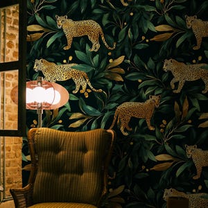 May include: A brown armchair with a patterned fabric sits in front of a dark green wall with a repeating pattern of gold leaves and leopards. A small wooden table with a brown ceramic pot sits in front of the chair.