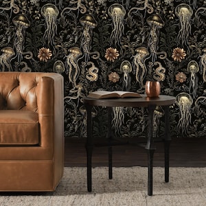 May include: A black and gold wallpaper with a repeating pattern of jellyfish and octopus tentacles. The wallpaper is displayed on a wall behind a brown leather sofa and a black metal side table with a book on top.