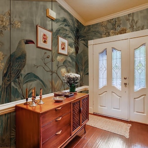 May include: An entrance hall with toucan and floral wallpaper. A wooden cabinet with drawers and a woven door panel is below framed artwork. The space includes a white door with glass panels and a red magazine holder.