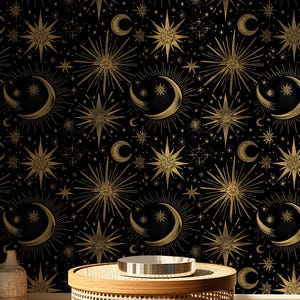 Può includere: Carta da parati nera con un motivo celeste dorato di lune, stelle e raggi di sole. Il design include lune crescenti, varie forme di stelle e piccoli punti. Un tavolino rotondo e intrecciato con un vassoio d'argento è posto davanti alla carta da parati.