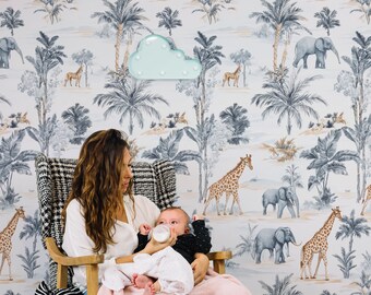 May include: A woman sits in a rocking chair with a baby in her arms. The baby is drinking from a bottle. The woman and baby are in front of a white wall with a jungle animal print wallpaper. The wallpaper features elephants, giraffes, palm trees, and a light blue cloud-shaped nightlight.