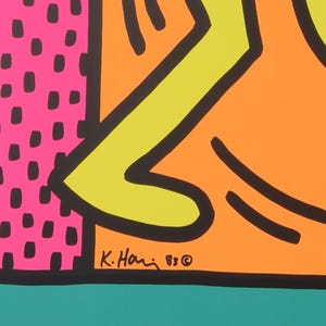 Puede incluir: Una impresi&oacute;n de arte abstracto colorida con un dise&ntilde;o amarillo, verde y naranja. La impresi&oacute;n est&aacute; firmada "K. Haring '83 &copy;" en la esquina inferior derecha.