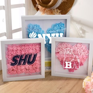 Puede incluir: Tres obras de arte florales enmarcadas. Una presenta rosas rosas con "SHU" en azul marino. Otra tiene un corazón de rosas rosas con un oso blanco y la letra "B". La tercera tiene rosas azules con texto blanco.