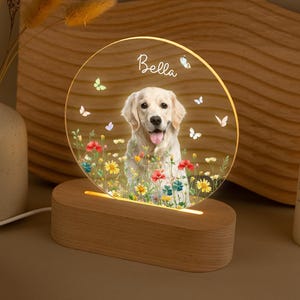 May include: A circular acrylic night light with a Golden Retriever dog design, flowers, and butterflies. The name "Bella" is written on the top. The light is set on a wooden base. The light is illuminated.
