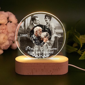 Könnte beinhalten: Ein runder, beleuchteter Foto-Display aus Acryl mit einem Schwarz-Weiß-Bild eines Paares. Das Display ist auf einem Holzsockel montiert. Der Text enthält "1985", "2025", "Martin & Jessica" und "50th Anniversary".