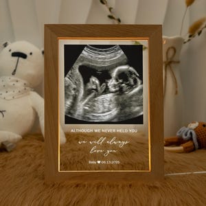 May include: Wooden framed illuminated ultrasound image. The image displays a grayscale sonogram of a baby. The frame includes the text: "ALTHOUGH WE NEVER HELD YOU, we will always love you. Baby 06.13.2025."