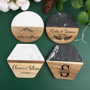 May include: Four personalised coasters with a marble and wood design. The coasters feature different names and dates, including "Gideon & Attica", "Kristen & Simon Est. 2022", "Chance & Selena 12.07.2023", and "Simon".