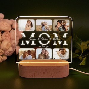 May include: A white acrylic photo frame with a wooden base. The frame has six photo slots and the word "MOM" in large letters with the names "Sarah", "Elvino", and "Heather" written below. The text "we love you" is written below the names.