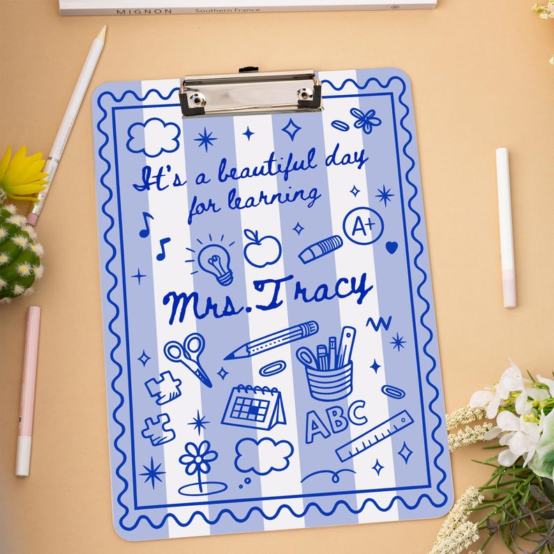 May include: A blue and white striped clipboard with a decorative border. The clipboard features the text "It's a beautiful day for learning" and "Mrs. Tracy" along with various school-themed doodles.