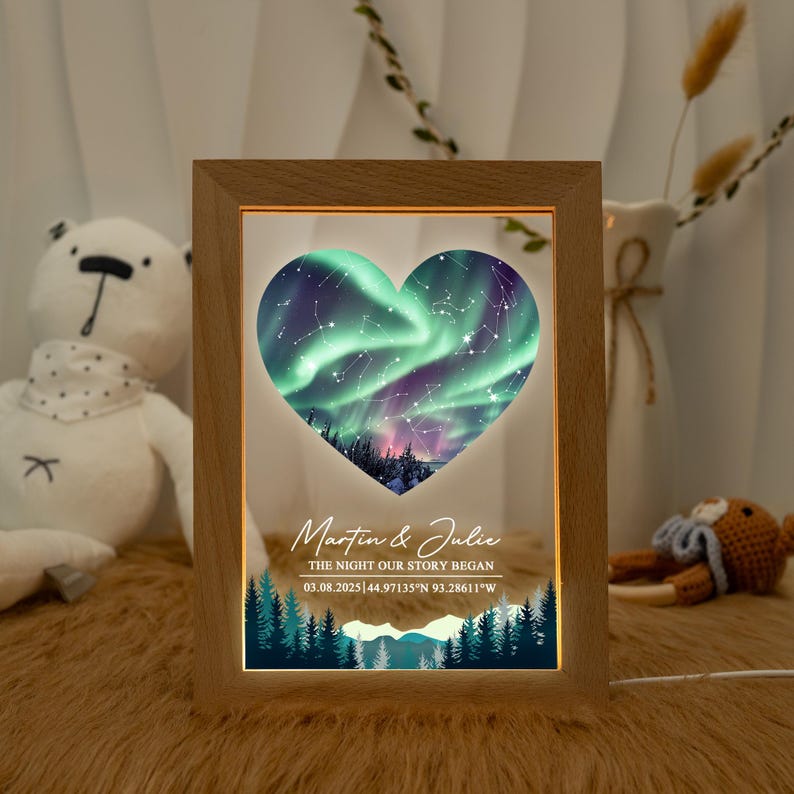 May include: A wooden framed night light with a heart-shaped design. The heart displays a green and purple aurora borealis scene with constellations. The text reads "Martin & Julie" and "THE NIGHT OUR STORY BEGAN 03.08.2025 44.97135&deg;N 93.28611&deg;W".