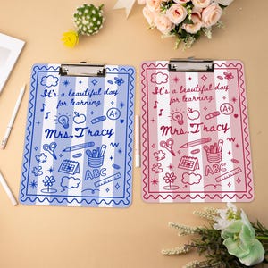 May include: Two clipboards with a school theme. One is blue with white stripes and the other is pink with white stripes. Each clipboard has the text "It's a beautiful day for learning" and "Mrs. Tracy". The clipboards have school-related graphics.
