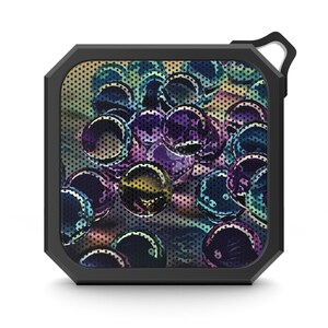 May include: Black square portable speaker with a colorful, abstract design of spheres in shades of purple, blue, and yellow. The speaker has a black frame and a small loop for hanging.