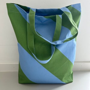 Könnte beinhalten: Eine große grüne und blaue gestreifte Tragetasche mit zwei langen Henkeln. Die Tasche ist aus robustem Stoff gefertigt und hat eine große Öffnung.