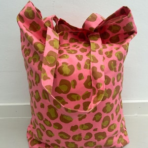 Könnte beinhalten: Eine rosa Tragetasche mit braunem Leopardenmuster. Die Tasche hat zwei lange Henkel.