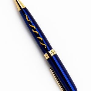 Puede incluir: Bolígrafo azul con detalles dorados. El bolígrafo presenta una punta, un clip y bandas decorativas doradas. Un diseño ondulado dorado adorna el cuerpo azul. El bolígrafo está sobre un fondo blanco.