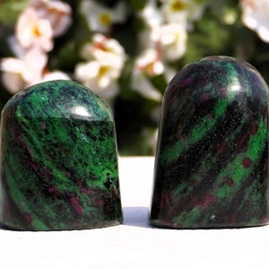 May include: Two green, black, and pink gemstone carvings shaped like rounded domes. The carvings are smooth and polished.