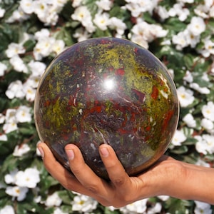 May include: A large, polished sphere of green, red, and black jasper. The sphere is smooth and has a high gloss finish.