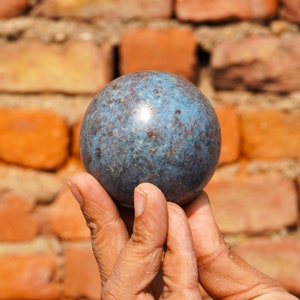 May include: A blue and brown sphere with a speckled pattern is held in a person's hand. The sphere is smooth and shiny.