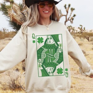 May include: A cream colored sweatshirt with a green Queen of Clubs playing card graphic. The card features a green shamrock design.