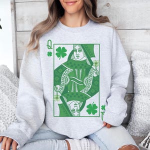 May include: A gray sweatshirt with a green Queen of Clubs playing card design. The card features a green shamrock and a woman with a crown.