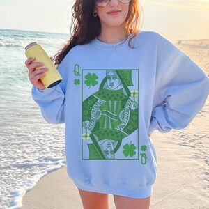 May include: Light blue sweatshirt with a green Queen of Hearts playing card graphic. The card features a green shamrock design and the text "Q" and "O".