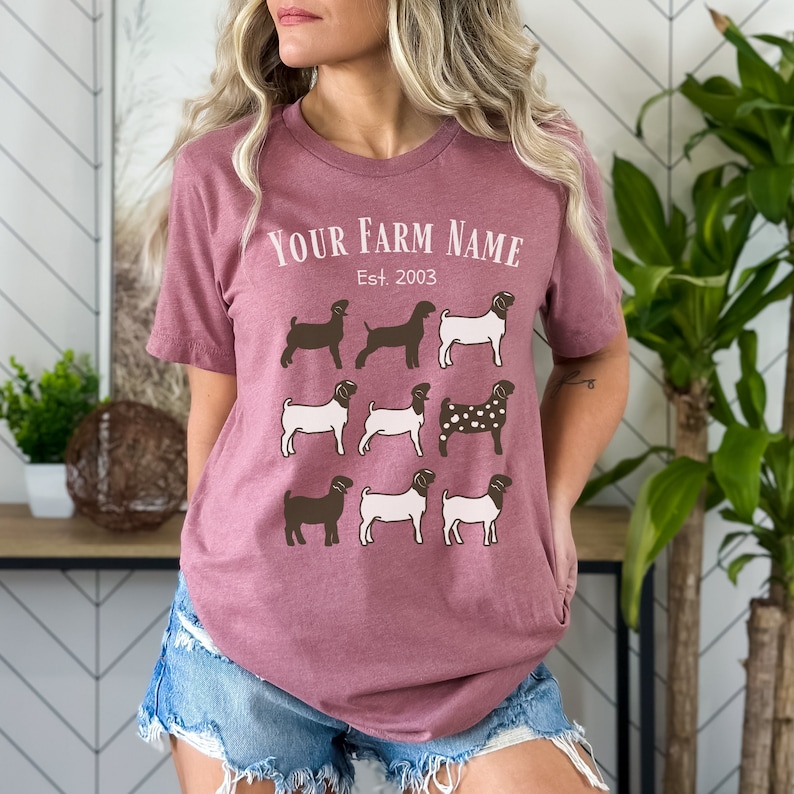 May include: A mauve t-shirt with a white graphic of goats and the text "YOUR FARM NAME Est. 2003".