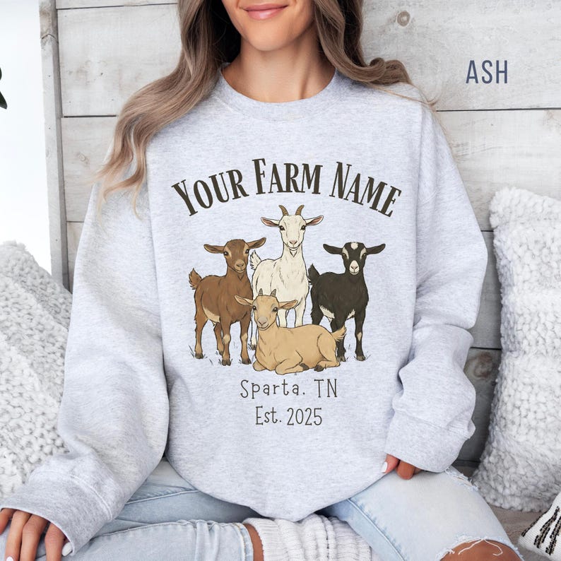 May include: Ash gray sweatshirt with a farm-themed graphic. The design features four goats in various shades of brown, white, and black, with the text "YOUR FARM NAME" above them. Below the goats, the text reads "Sparta, TN Est. 2025".