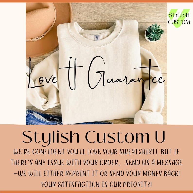 May include: Cream-colored sweatshirt with the text "Love It Guarantee" in black script. The sweatshirt is folded on top of blue jeans. A brown hat and a small succulent plant are also visible. The text "Stylish Custom U" is at the bottom.