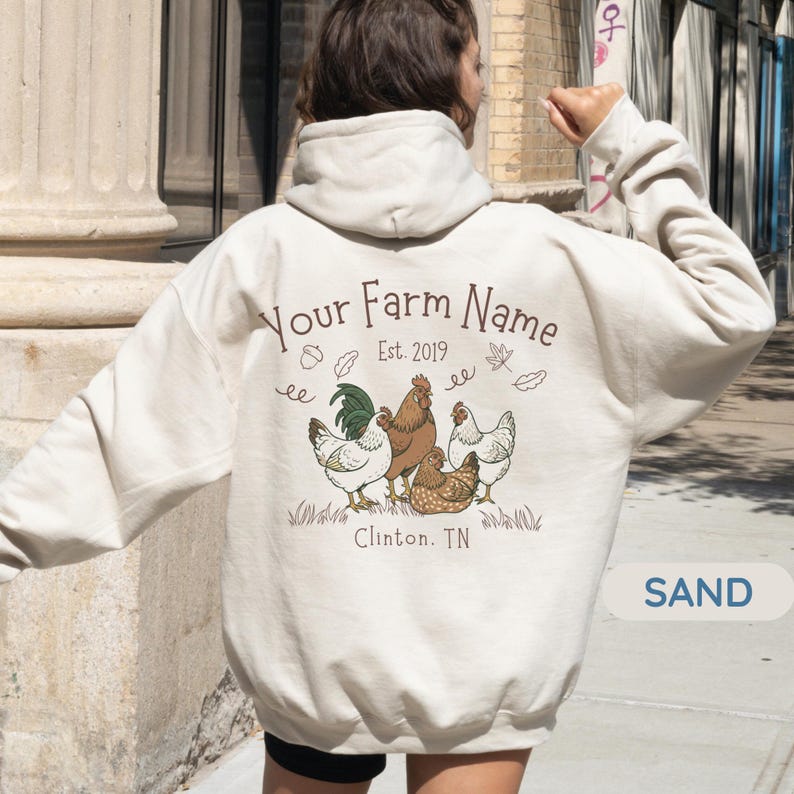 May include: Sand-colored hoodie with a drawstring hood. The back features a graphic of a rooster and hens, with the text "Your Farm Name Est. 2019 Clinton, TN". The design includes leaves and grass.
