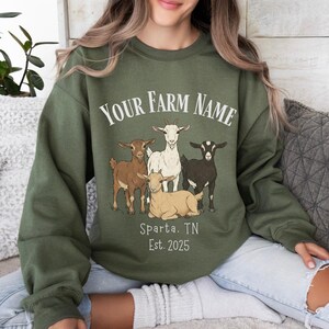May include: Olive green sweatshirt with a graphic of five goats in various colors. The text "YOUR FARM NAME" is arched above the goats, with "Sparta, TN Est. 2025" below. The sweatshirt is a crew neck style.