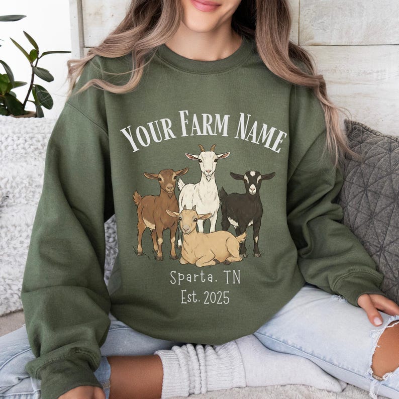 May include: Olive green sweatshirt with a graphic of five goats in various colors. The text "YOUR FARM NAME" is arched above the goats, with "Sparta, TN Est. 2025" below. The sweatshirt is a crew neck style.