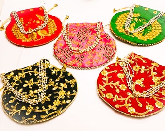 Puede incluir: Cinco bolsas redondas con cordón en rojo, verde, rosa y negro, cada una con intrincados bordados dorados, motivos florales o de pavo real, y un asa decorativa de cuentas blancas. Las bolsas están dispuestas en grupo, mostrando colores variados y un trabajo detallado de hilo metálico en las superficies de tela.
