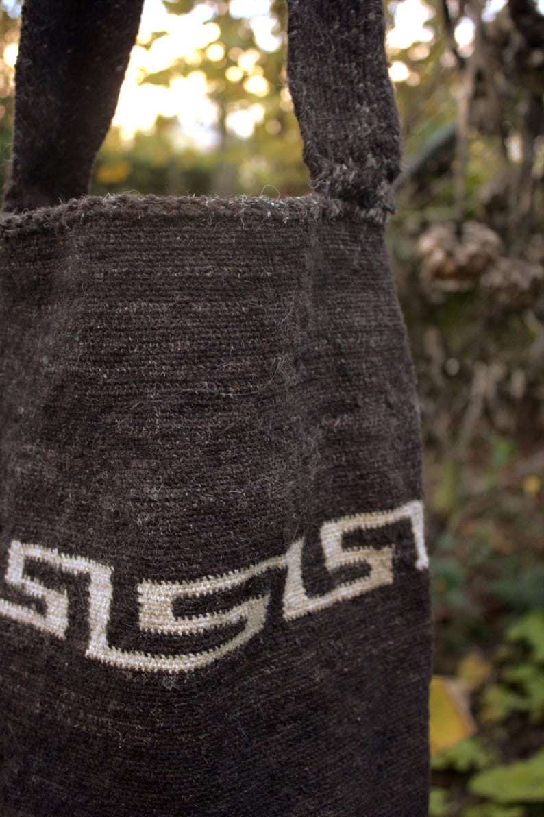 Puede incluir: Una bolsa tejida marr&oacute;n con un dise&ntilde;o geom&eacute;trico blanco. La bolsa tiene dos asas y est&aacute; hecha de una tela gruesa y texturizada.