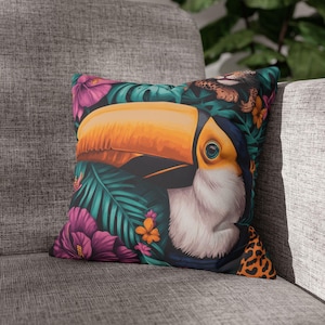 Puede incluir: Cojín decorativo cuadrado con un tucán con un gran pico naranja, rodeado de flores y follaje tropicales en tonos rosa, turquesa y naranja. El cojín tiene un fondo negro y un estampado de leopardo.