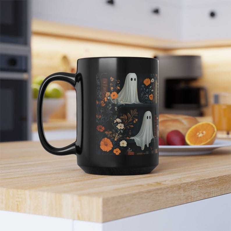 A black mug with a Halloween-themed design featuring ghostly figures and floral patterns is placed on a wooden table in a kitchen setting.