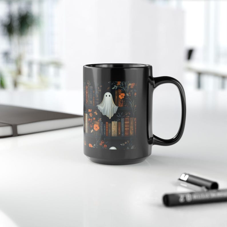 A black mug with a Halloween-themed design featuring a ghost, flowers, and books on a white background.